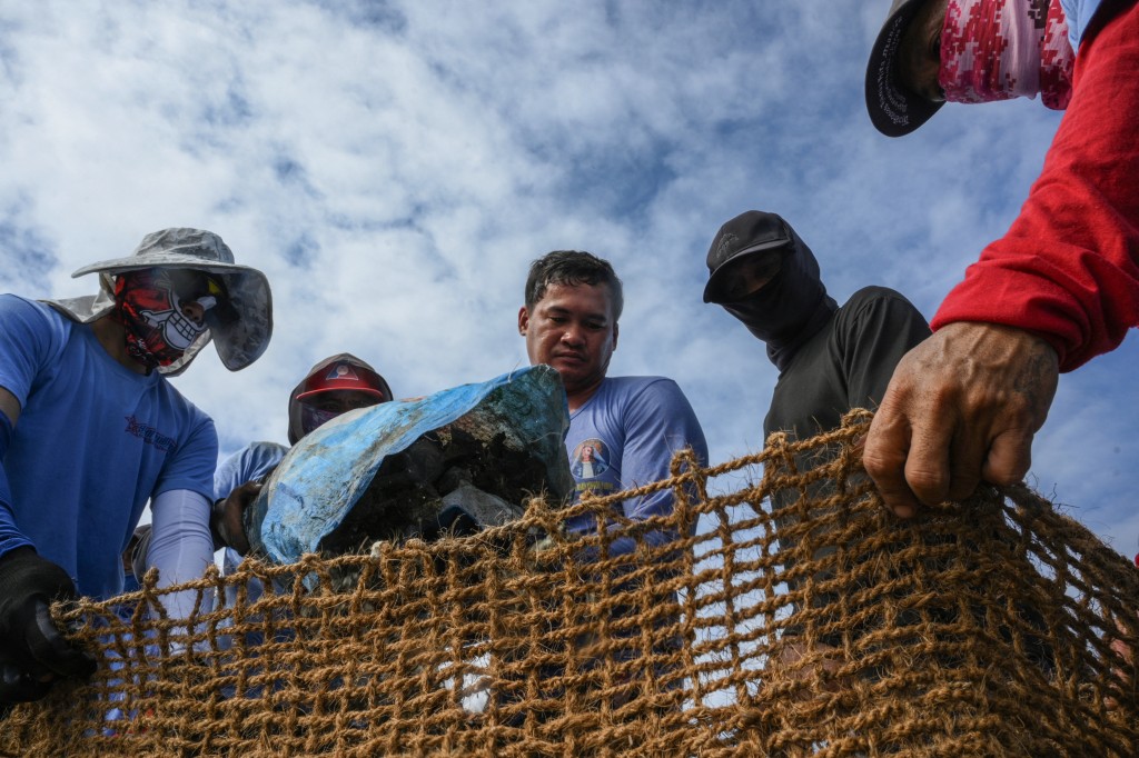 Photo by TED ALJIBE / AFP  In this photo taken on October 13, 2026, workers fill coconut-fibre bags with oyster shells on a breakwater at Pamarawan Island in Malolos City, Bulacan province.