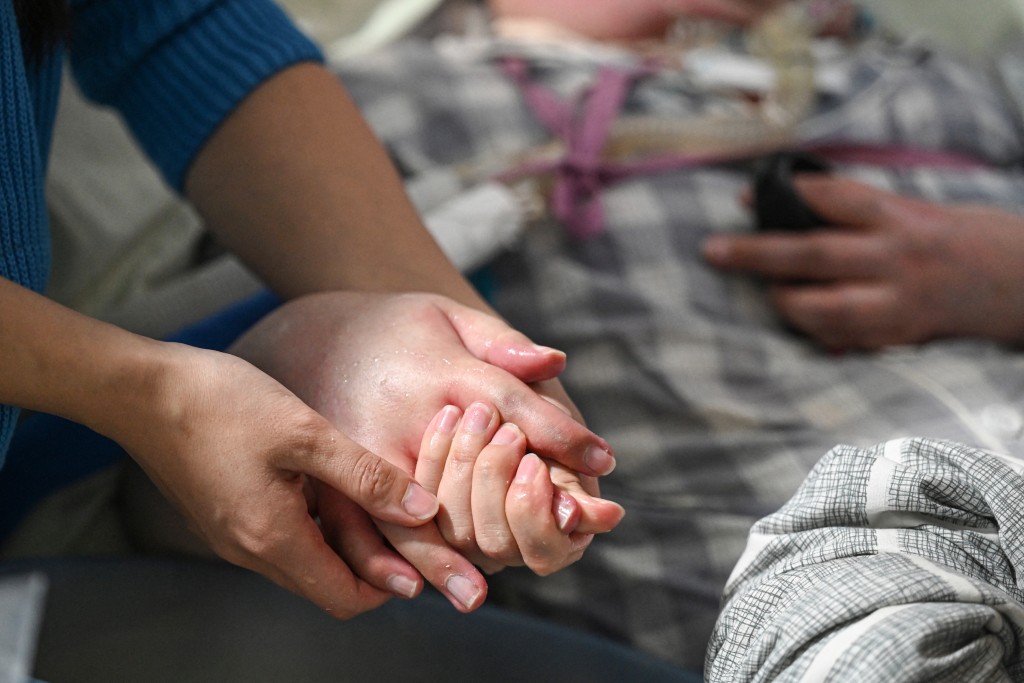 Photo by JADE GAO / AFP  This photo taken on December 16, 2025 shows Li Qian, cleaning the hand of her elder brother Li Xia, who has Duchenne muscular dystrophy, at their house in southwestern China's Chongqing municipality.