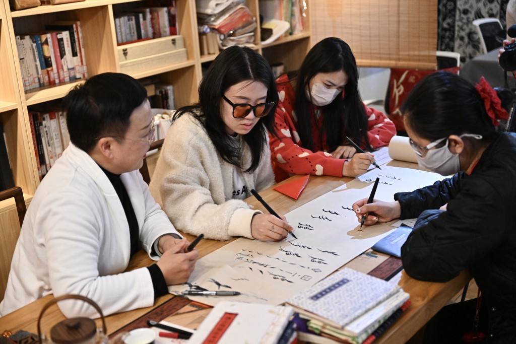This picture taken on April 14, 2025 shows Xu Yan (L) teaching students to write Nushu characters during a workshop in Beijing. Nushu, "female script", was created around 400 years ago when women were still barred from attending school. (Photo by Pedro PARDO / AFP)