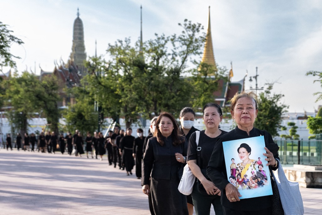 Mourners hold portraits of Thailand's former Queen Sirikit as they line up to pay respects to the late queen at the Grand Palace in Bangkok on October 26, 2025. (AFP)