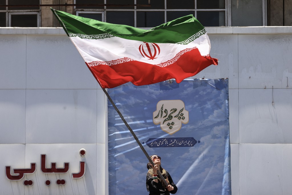 Photo by ATTA KENARE / AFP  An Iranian woman waves a national flag at Valiasr Square in Tehran on June 15, 2026.