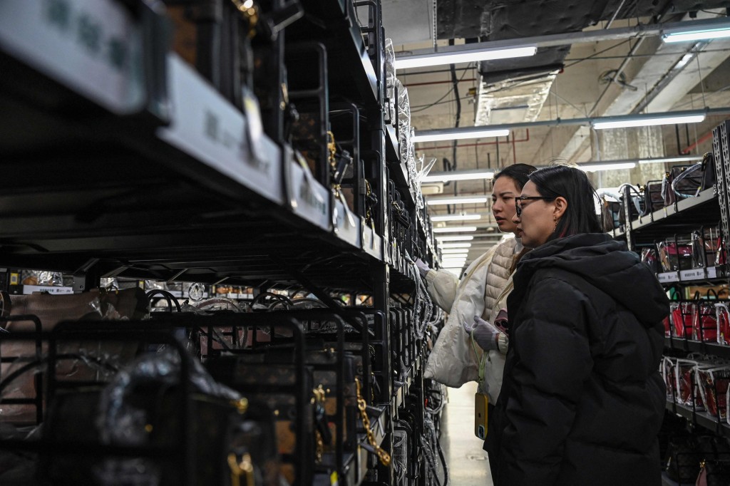 The photo taken on February 10, 2026 shows people browsing through luxury bags at a second-hand store in Shanghai. Boosting domestic consumption will be among key goals set forth by China's leaders at the annual Two Sessions political conclave this week, but they face an uphill battle. (Photo by Jade GAO / AFP)