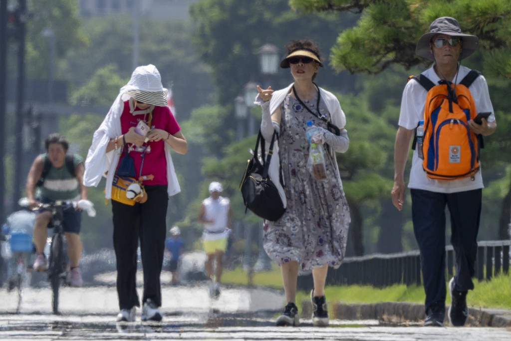 Foreign tourists walk in the hot sun on a sidewalk near the Imperial Palace in Tokyo on August 6, 2025. Japan logged a new heat record on August 5, with the mercury hitting 41.8C, the weather office said, warning temperatures may rise further still. (Photo by Kazuhiro NOGI / AFP)
