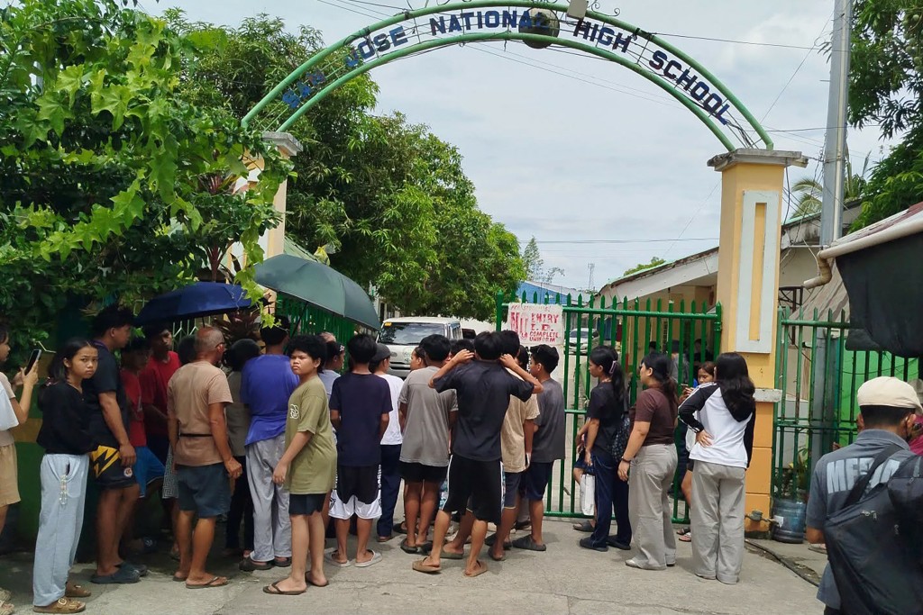 Photo by NOEL SIANOSA / AFP Students and their parents wait for permission from school authorities to enter the school compound at the gate of San Jose High School in Tacloban City, Leyte province in the central Philippines on June 23, 2026, a day after a shooting incident.