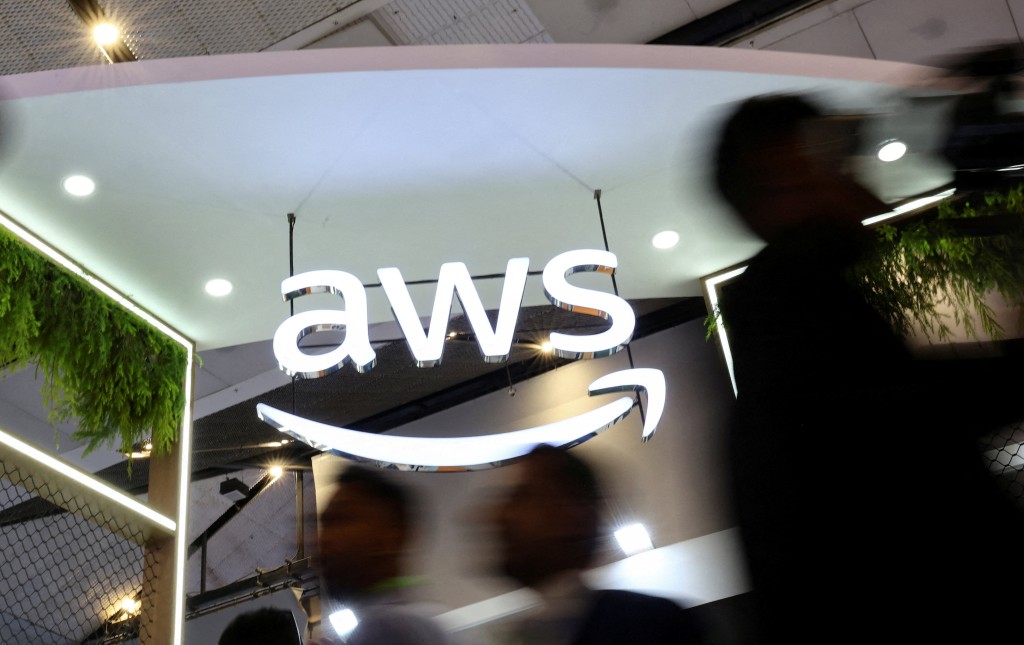 People walk past the logo of Amazon Web Services (AWS) at its exhibitor stall at the India Mobile Congress 2025 at Yashobhoomi, a convention and expo center in New Delhi, India, October 8, 2025. (Reuters)