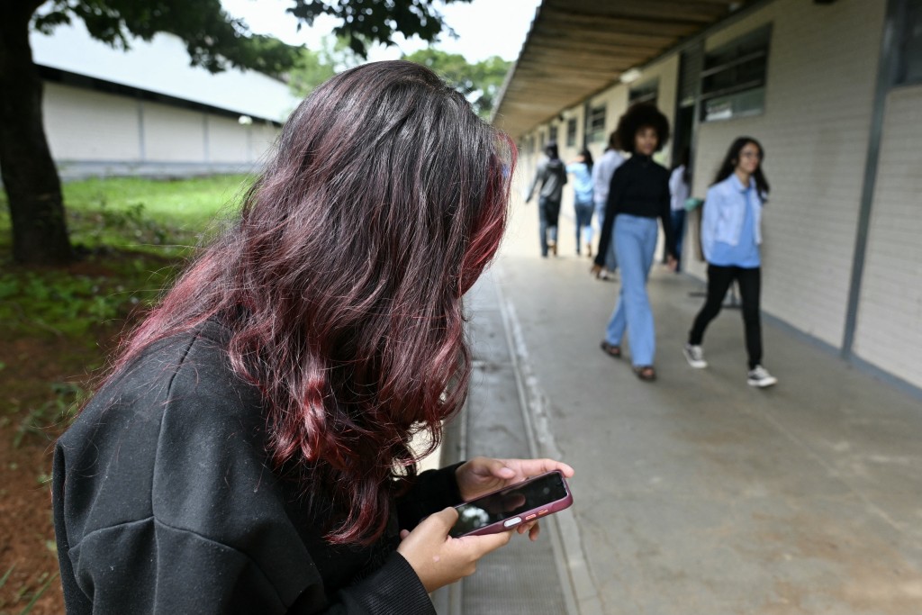 Photo by EVARISTO SA / AFP. A young student uses her mobile phone at a public school in Planaltina, Brasilia on March 16, 2026.