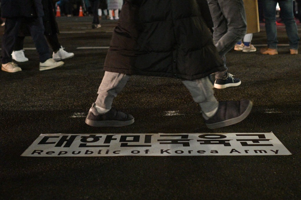 Photo by ANTHONY WALLACE / AFP  In this file photo taken early on December 4, 2024, people walk past an army sign on the ground as they gather outside the National Assembly in Seoul, after then South Korea president Yoon Suk Yeol declared martial law.