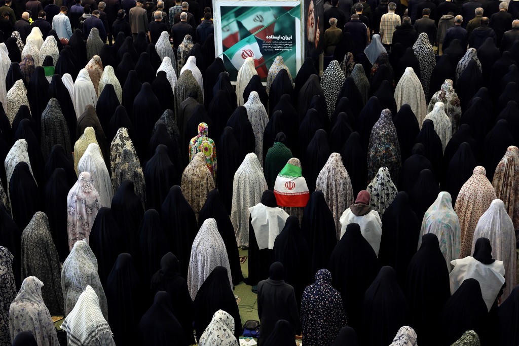 Photo by STR / AFP. Iranian Shia women, including one covered in the Iranian national flag, take part in Eid al-Fitr prayers, marking the end of the Muslim holy month of Ramadan, at the Grand Mosalla mosque in Tehran on March 21, 2026.