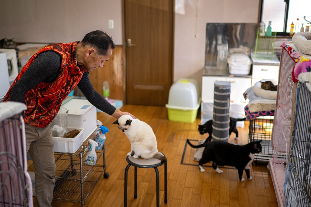 Photo by PHILIP FONG / AFP  This picture taken on March 5, 2026 shows former nuclear plant worker Toru Akama petting a cat at his animal shelter in Namie, Fukushima prefecture.