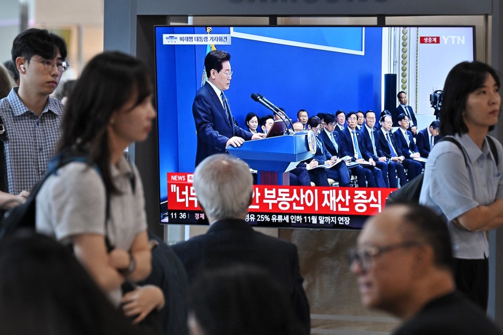 People walk by a television screen showing a YTN news broadcast of South Korean President Lee Jae-Myung holding a press conference at the Blue House, at a train station in Seoul on September 18, 2026. (Photo by Lillian SUWANRUMPHA / AFP)