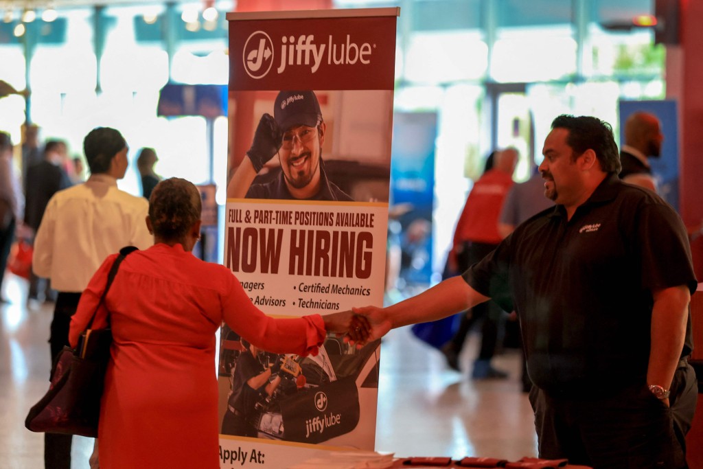 A 'Now Hiring' sign sits next to the Jiffy Lube booth during the Mega JobNewsUSA South Florida Job Fair held in the Amerant Bank Arena on April 30, 2025 in Sunrise, Florida. AFP