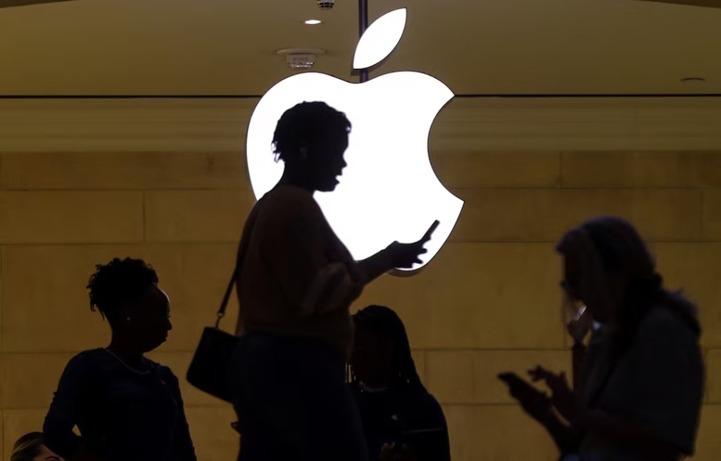 A women uses an iPhone mobile device as she passes a lighted Apple logo at the Apple store at Grand Central Terminal in New York City, U.S., April 14, 2023. REUTERS/Mike Segar/ File Photo