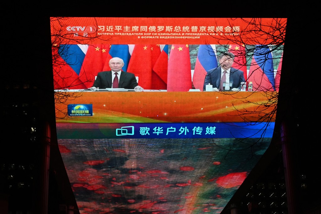 Russian President Vladimir Putin (L) and Chinese President Xi Jinping are seen during news coverage about a video call between the two leaders, on a giant screen outside a shopping mall in Beijing on February 4, 2026. (AFP)
