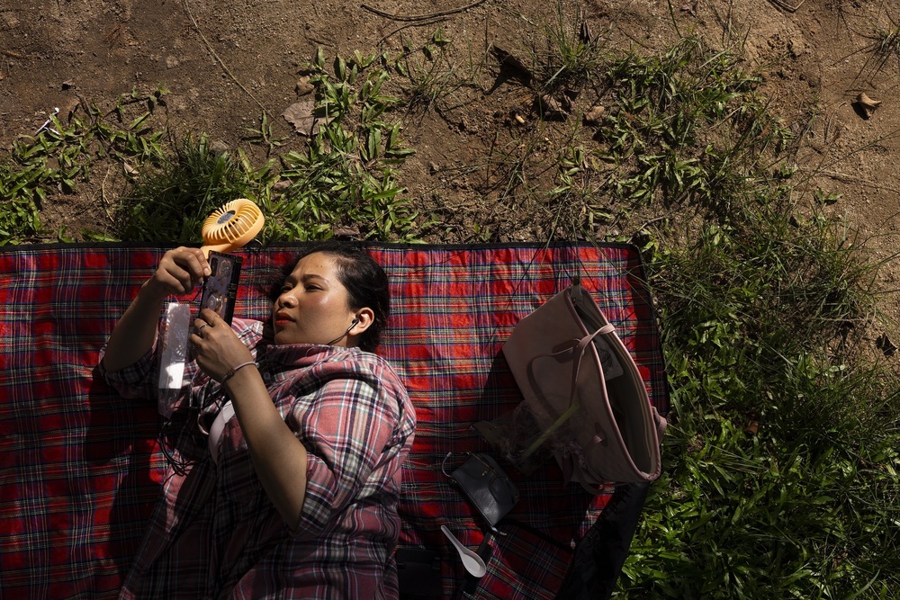 Isdalia, 41, domestic worker, browses her phone as she holds a portable fan at a park during her day off amid the summer heat in Hong Kong, Sunday, Aug. 6, 2023. (AP)