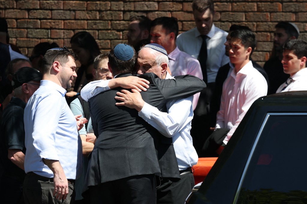 Photo by DAVID GRAY / AFP  Mourners hug after the funeral of Boris and Sofia Gurman, who were killed in the December 14 Bondi Beach shooting attack, at the Sydney Chevra Kadisha in Sydney on December 19, 2025.