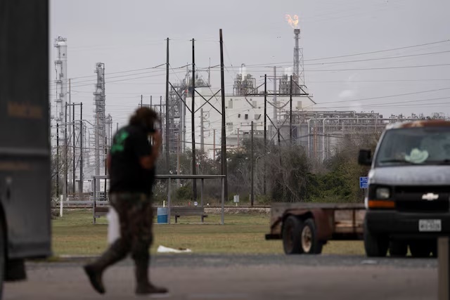 A man passes by at an Exxon gas station as a flare stack burns in the distance at the Formosa Point Comfort Plant in Point Comfort, Texas, U.S., January 8, 2026. REUTERS/Antranik Tavitian/File Photo