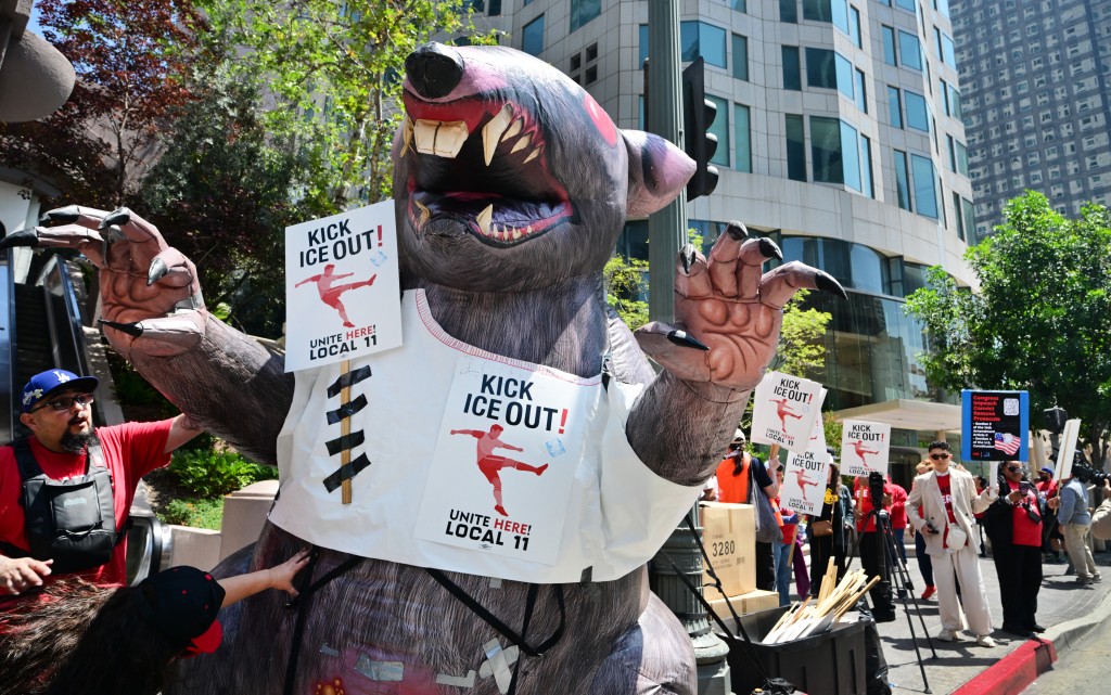 Photo by FREDERIC J. BROWN / AFP  "Kick ICE Out" signs are placed on an infaltable rat as SOFI stadium workers protest outside FIFA World Cup 26 Los Angeles Office calling for ICE to be banned from the World Cup on May 1, 2026.