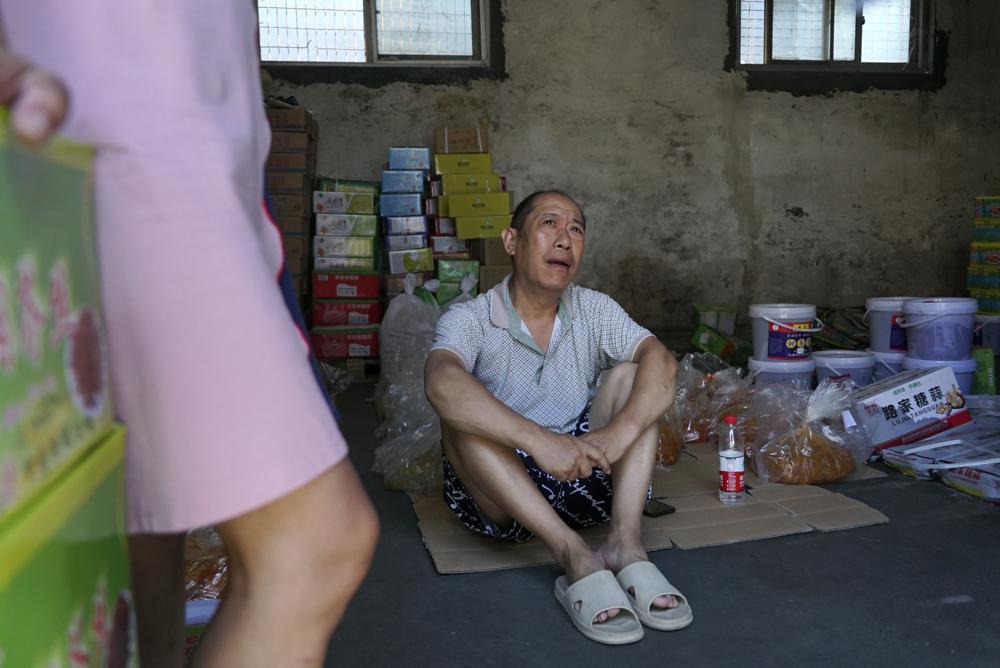 Lu Jinling sits in a family warehouse with pickled vegetables that he and his wife salvaged from the floods in Xinxiang in central China's Henan Province, Monday, July 26, 2021. 