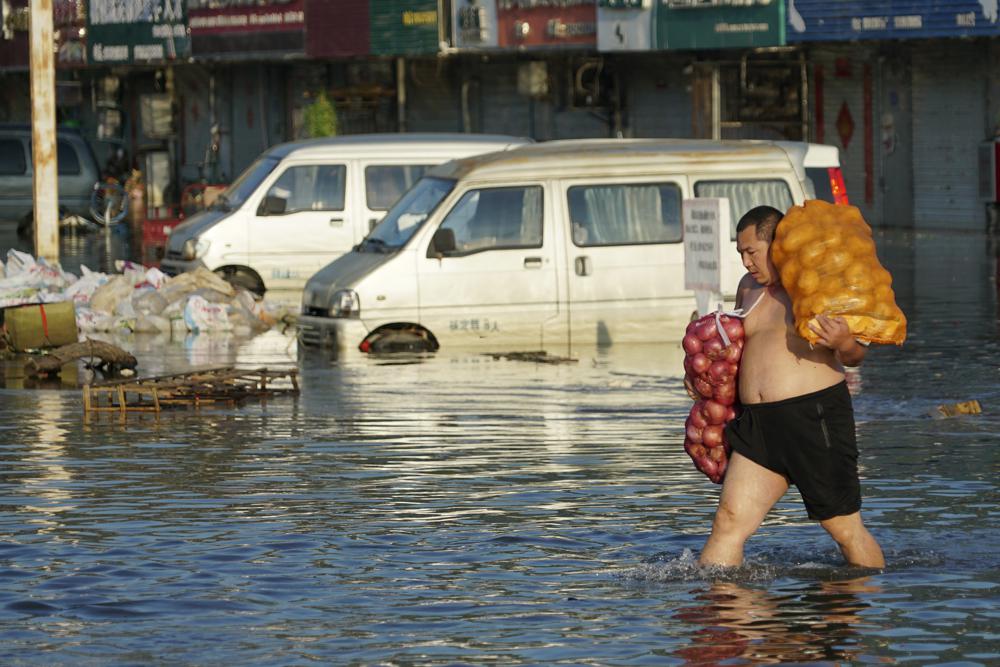 A man carries bags of onions out of the flooded Yubei Agricultural and Aquatic Products World in Xinxiang in central China's Henan Province, Monday, July 26, 2021. Record rain in Xinxiang last week left the produce and seafood market soaked in water. 
