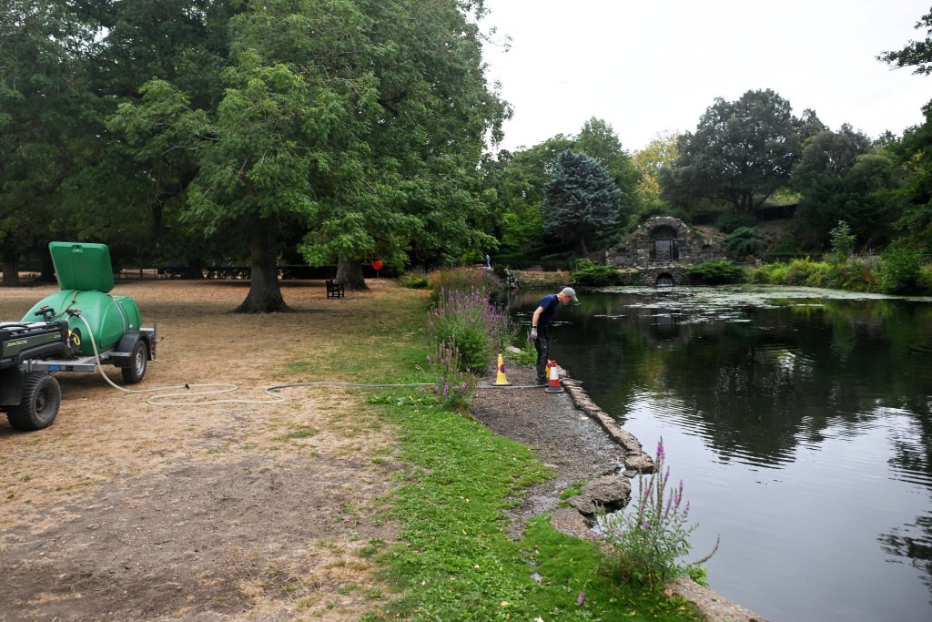 Photo by JUSTIN TALLIS / AFP  This photo taken on August 18, 2026 shows specialist volunteer Chris Poole looking into a lake while pumping water into a bowser at Chiswick House in west London.