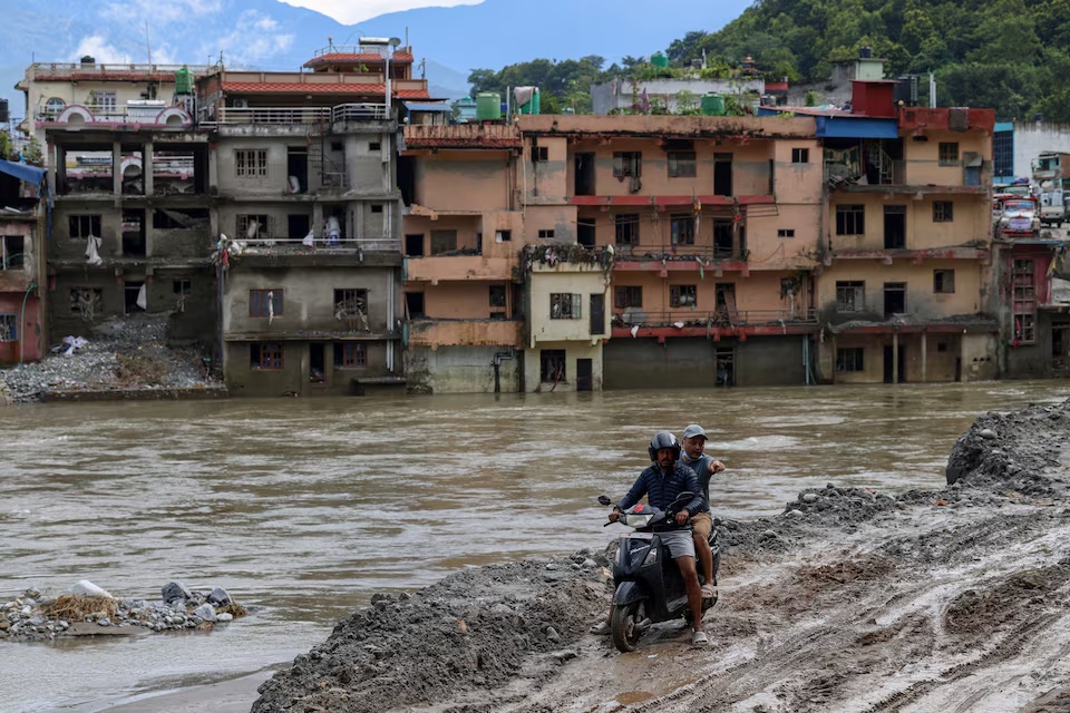 A motorcyclist rides through thick mud with flood-damaged houses in the background following deadly flash floods and a mudslide, in Devighat, Nuwakot district, Nepal, September 11, 2026. REUTERS/Tyrone Siu/File Photo