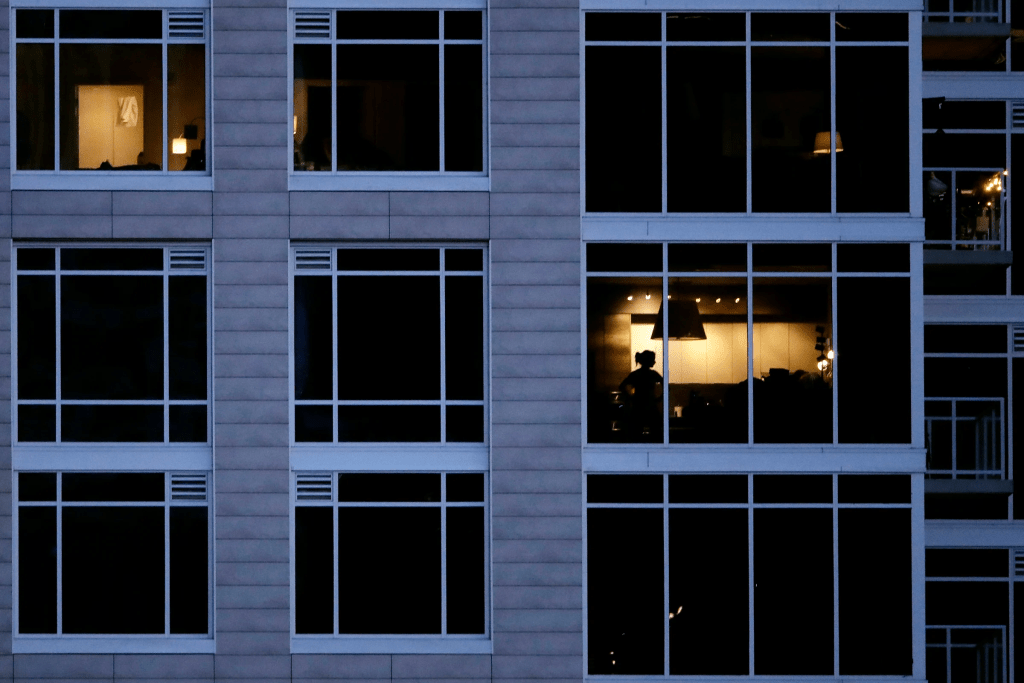 FILE - A person looks out of a window in an apartment building in Kansas City, Mo., May 3, 2020. (AP Photo/Charlie Riedel, File)