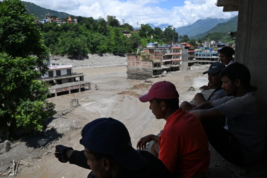 Photo by ARUN SANKAR / AFP People watch from a rooftop as houses lie deluged in sludge after flash floods at Trishuli in Nepal's Nuwakot district on August 27, 2026.