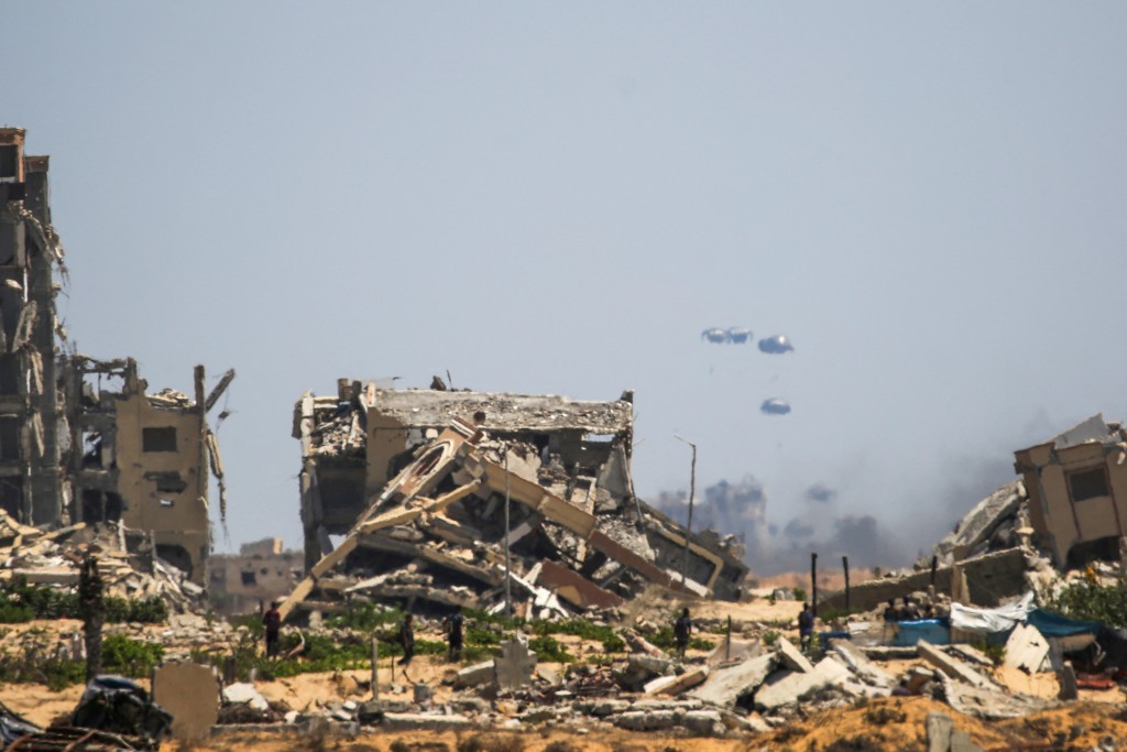 Palestinians rush to the site where parachuted aid packages are landing in the Nuseirat area in the central Gaza Strip during an airdrop above the Israel-besieged Palestinian territory on August 6, 2025.