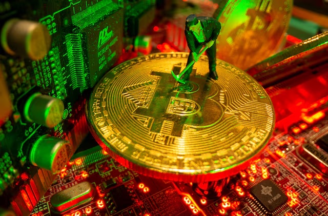 A small toy figure and representations of the virtual currency bitcoin stand on a motherboard in this picture illustration taken May 20, 2021. REUTERS/Dado Ruvic/Illustration/File Photo