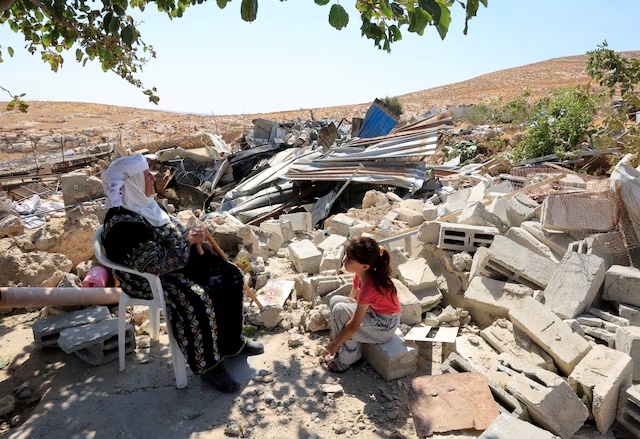 A Palestinian woman and a child sit amid the rubble after Israeli heavy machinery demolished homes in Jinba village in Masafer Yatta, near Hebron, in the Israeli-occupied West Bank, September 23, 2026. REUTERS/Mussa Qawasma