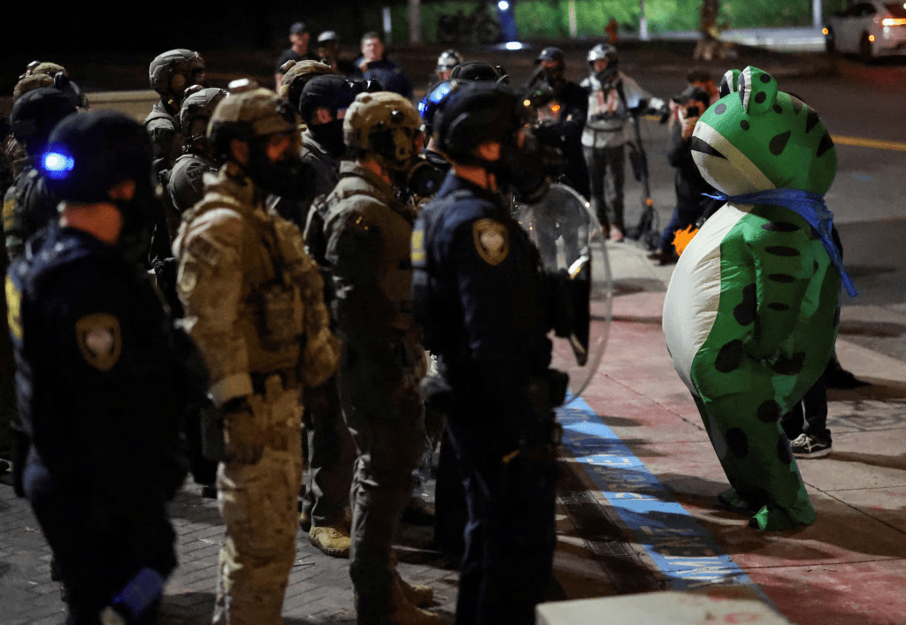 A demonstrator dressed in an inflatable frog costume stands infront of law enforcement officers during a protest outside of the ICE (Immigration and Customs Enforcement) headquarters in south Portland, Oregon, U.S., October 3, 2025. REUTERS/Carlos Barria 