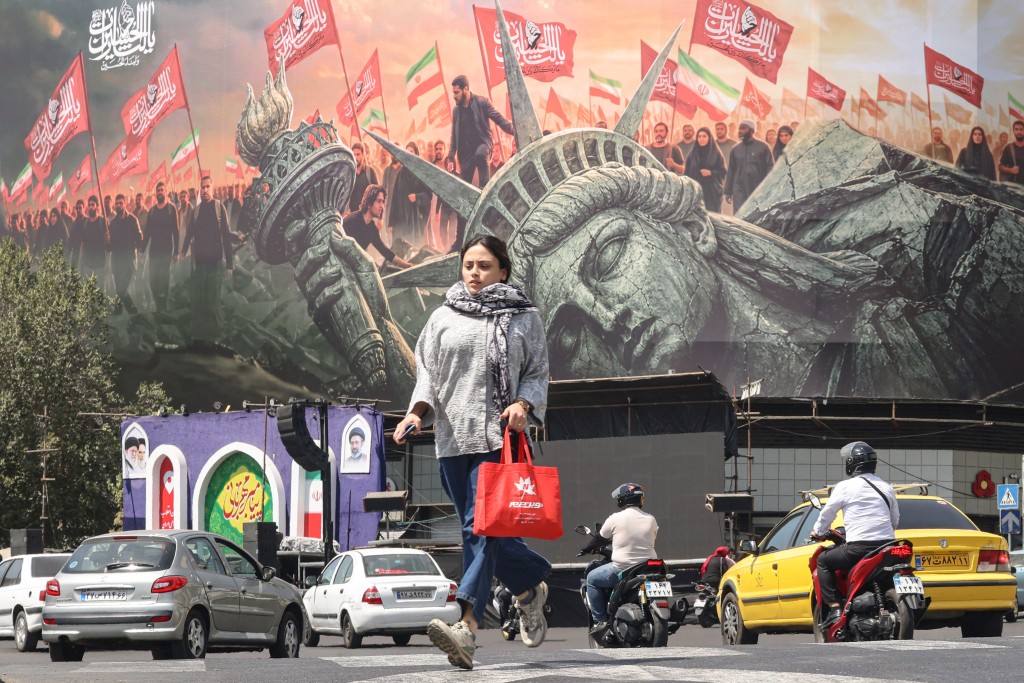 Photo by ATTA KENARE / AFP  A woman crosses as motorists drive past an anti-US billboard at Enghelab Square in Tehran on September 2, 2026.