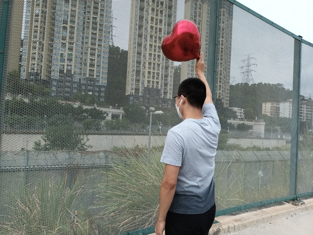 A man waves a balloon to his partner across the Shenzhen River from the Heung Yuen Wai land border control point. A man waves a balloon to his partner across the Shenzhen River from the Heung Yuen Wai land border control point.