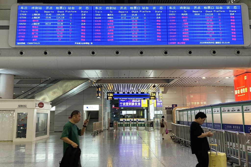 Passengers walk under a departure board at Ningbo railway station as most trains are cancelled due to approaching Typhoon Dolphin on August 9, 2026. (AFP)