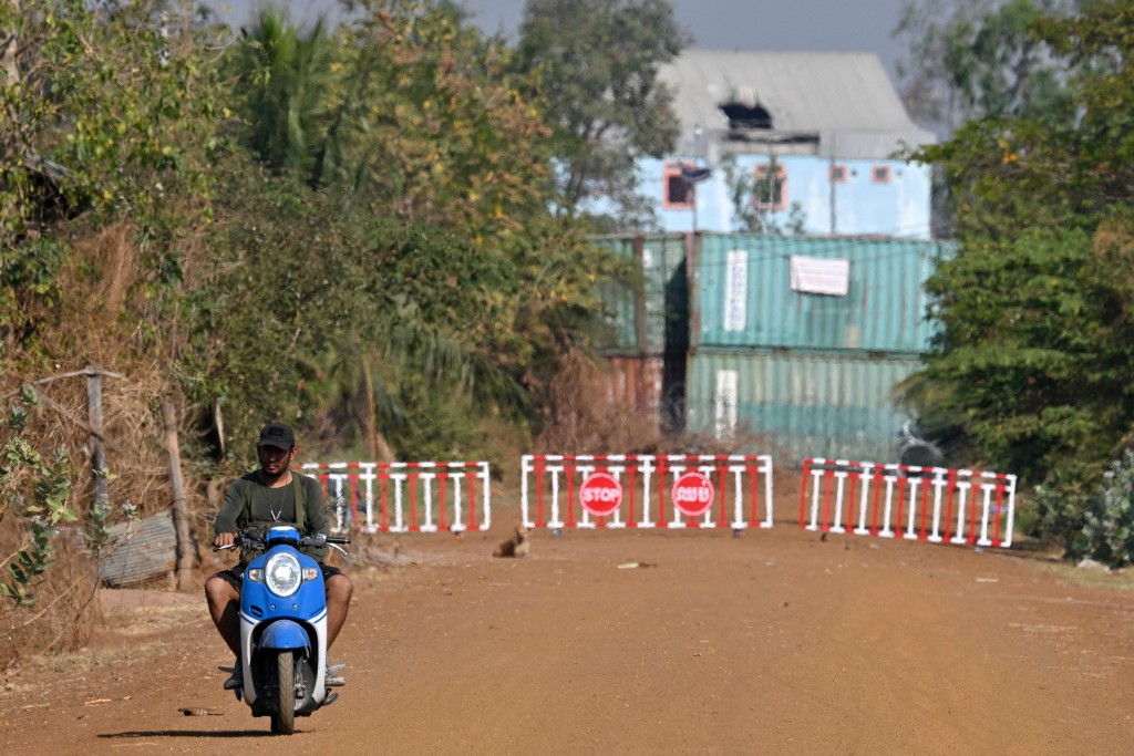 Photo by TANG CHHIN SOTHY / AFP  A man rides a motorcycle near shipping containers and barbed wire, installed by Thai forces, in Chouk Chey village in Banteay Meanchey province on February 5, 2026.