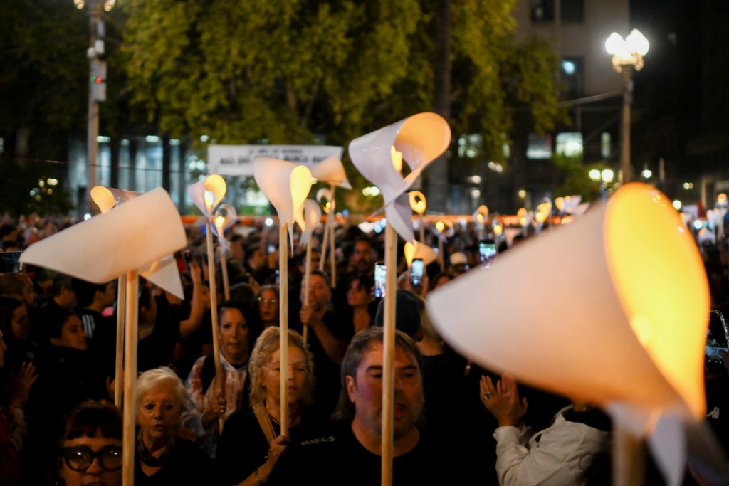 People hold illuminated white scarves as they gather in the Plaza de Mayo square in Buenos Aires on March 23, 2026, to attend a vigil one day before the 50th anniversary of the military coup that ushered in the military dictatorship (1976–1983). (Photo by Luis ROBAYO / AFP)