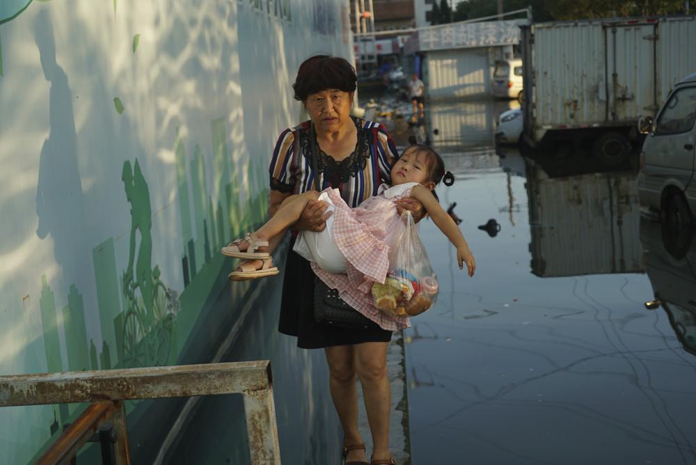 A woman carries a child in her arms as she walks on a curb above floodwaters in Xinxiang in central China's Henan Province, Monday, July 26, 2021. 