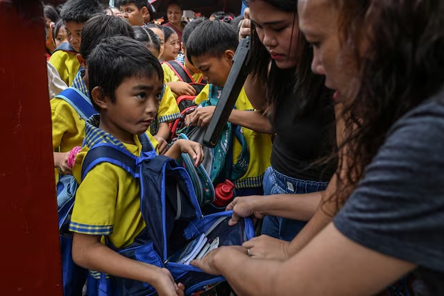 A parent assists in the checking of students' bags as they enter President Corazon Aquino Elementary School, a day after at least three students were killed and seven others injured when two students, aged 15 and 14, opened fire at a school in the city of Tacloban southeast of Manila, in Quezon City, Philippines, June 23, 2026. REUTERS/NOEL CELIS