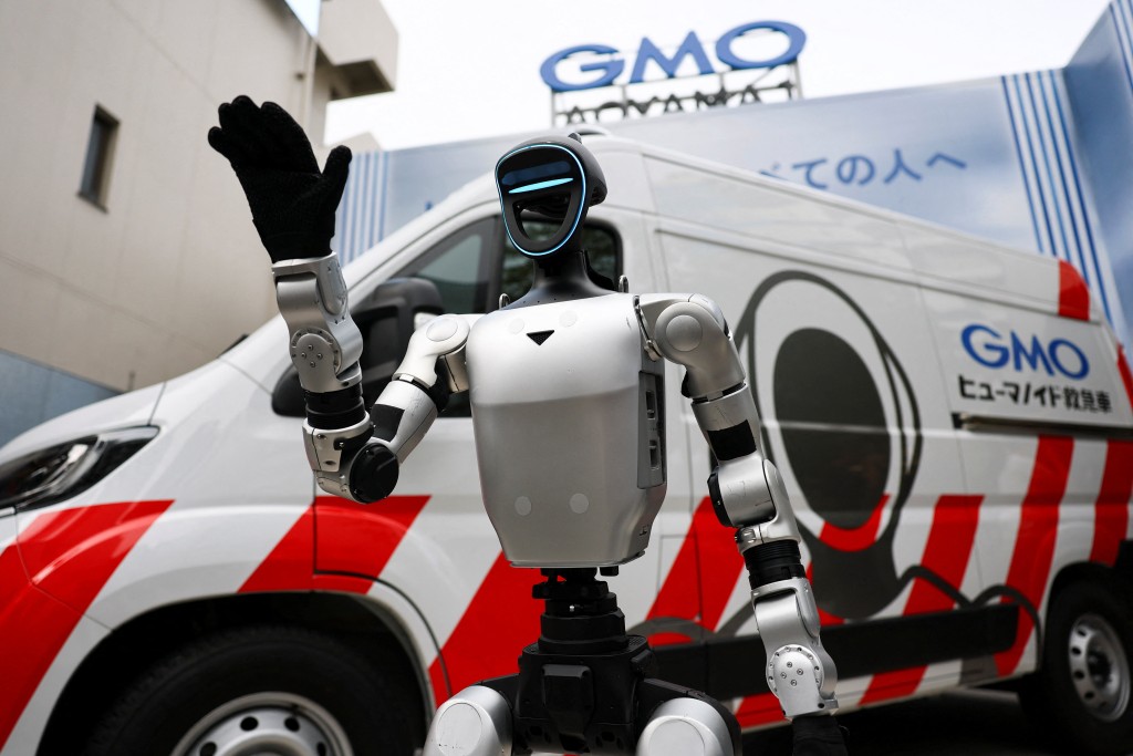 An Unitree G1 Humanoid Robot waves in front of a maintenance vehicle dedicated to humanoid robots called "GMO Humanoid Ambulances", specialized vehicles that rush to the scene of malfunctions or issues with humanoid robots to perform on-site diagnostics and repairs, or to provide replacement equipment, during an uveiling event to announce new services by GMO AI & Robotics Corporation (GMO AIR) in Tokyo, Japan, September 8, 2026.  REUTERS