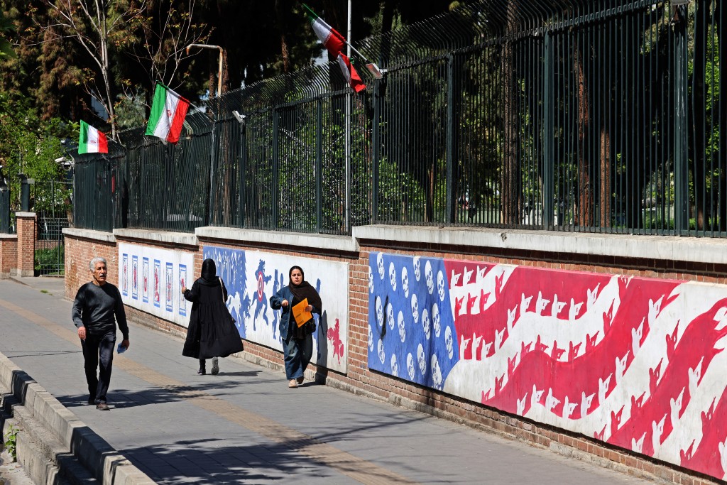 Photo by ATTA KENARE / AFP People walk past anti-US murals near the former US embassy in Tehran on April 11, 2026.