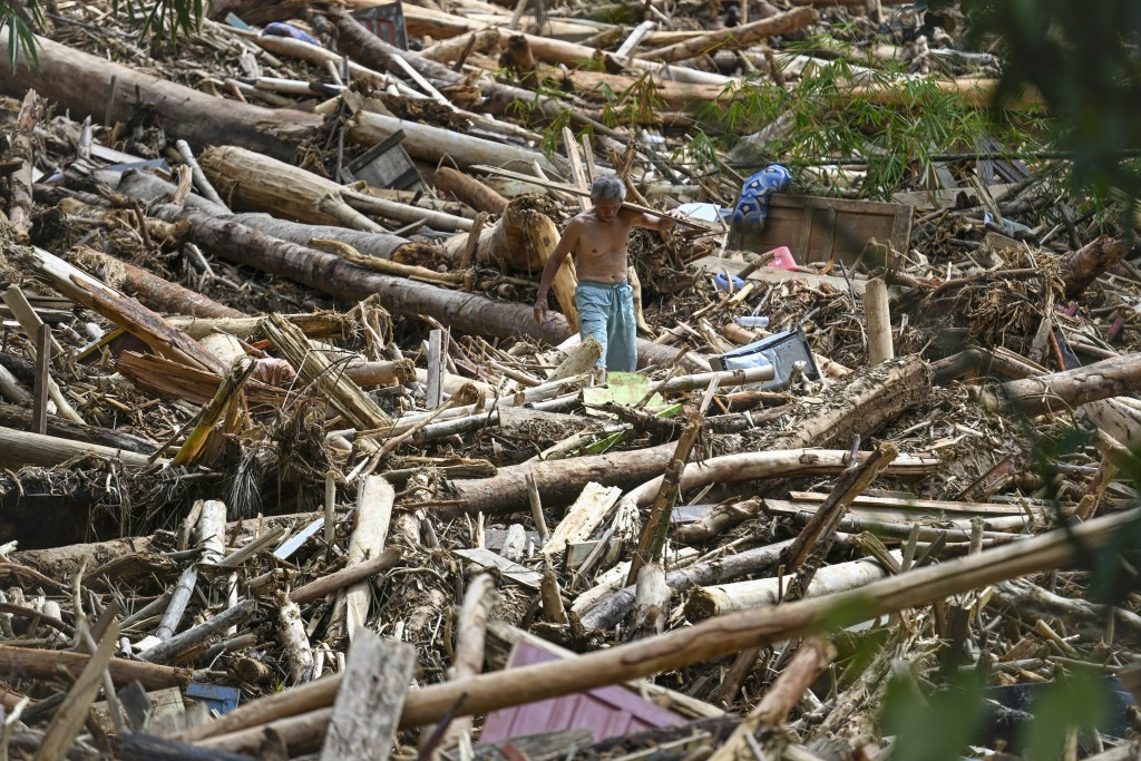 Photo by YT HARIONO / AFP  A villagers affected by flash floods walks amongst a pile of logs at Tukka village, Central Tapanuli, North Sumatra province, on December 2, 2025.