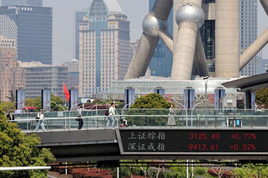 An electronic board shows Shanghai and Shenzhen stock indices as people walk on a pedestrian bridge at the Lujiazui financial district in Shanghai, China April 8, 2025. REUTERS