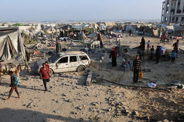 Palestinians stand near a damaged vehicle at the site of an overnight Israeli air strike on a house, in Khan Younis in the southern Gaza Strip, July 28, 2025 [Ramadan Abed/Reuters]