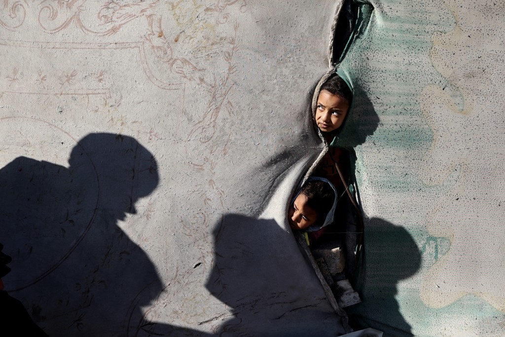 Photo by EYAD BABA / AFP  Children look on from a shelter in the Nuseirat camp for displaced Palestinians in the central Gaza Strip on December 22, 2025.