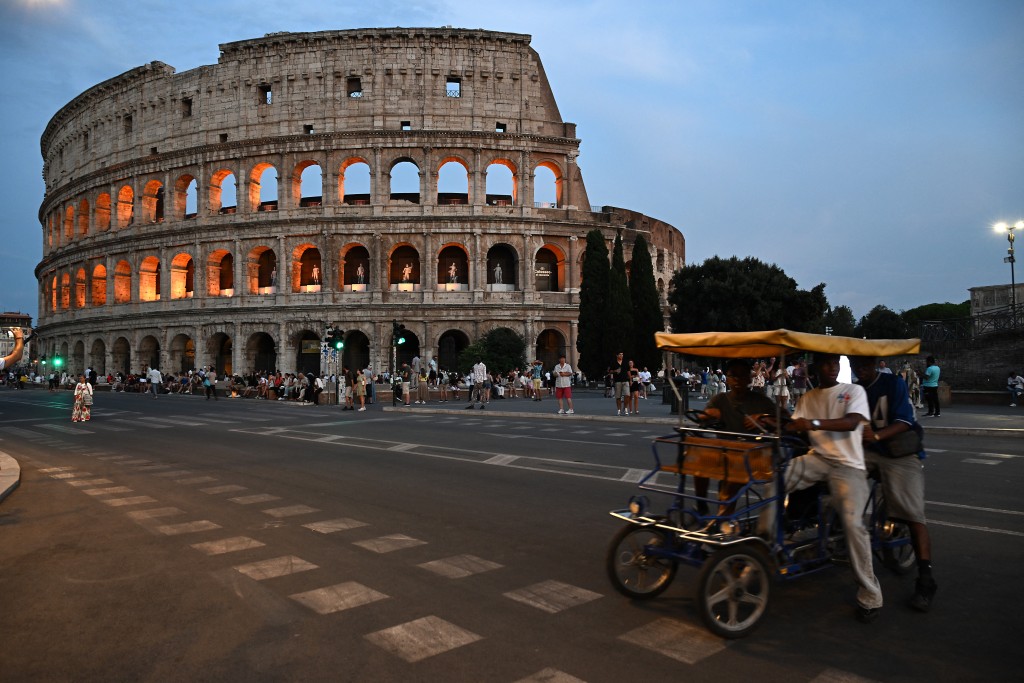 Photo by ANDREAS SOLARO / AFP Pedestrians walk past the Ancient Colosseum during "A Night at the Colosseum" tour, a guided visit, lasting approximately 60 minutes that winds through the monument’s first tier, the arena floor, and the underground areas, in central Rome on August 13, 2026.