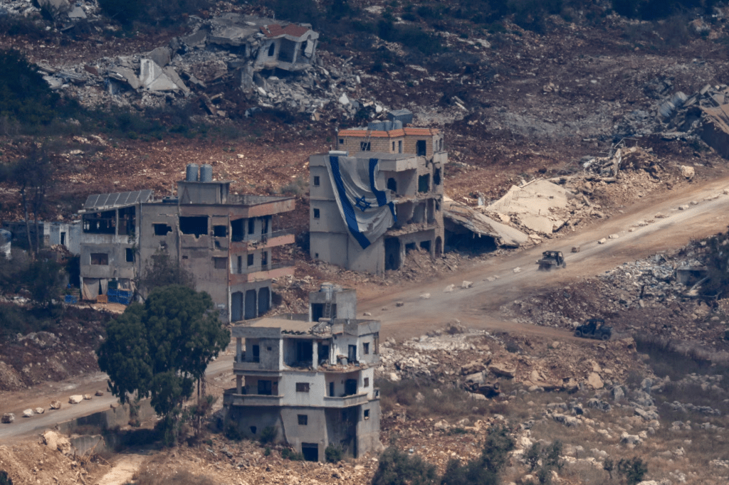 An Israeli military vehicle drives near a damaged building with a large Israeli flag in Lebanon, after Israel and Lebanon signed a framework agreement following U.S.-mediated talks, as seen from northern Israel, June 27, 2026. REUTERS/Amir Cohen 