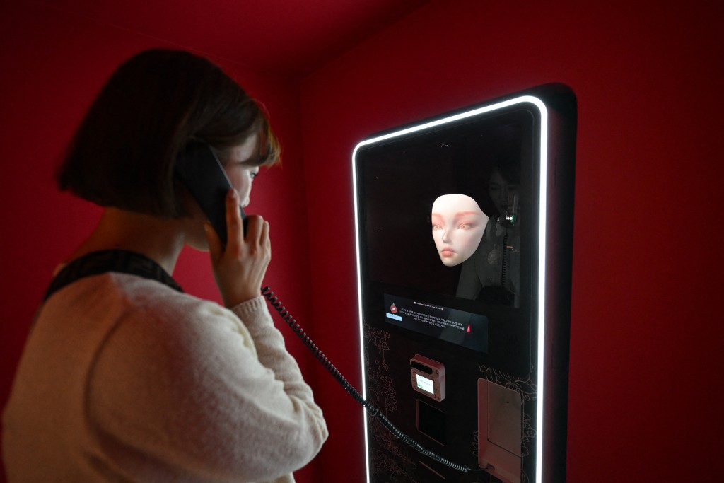 Photo by JUNG YEON-JE / AFP  This picture taken on April 15, 2026 shows a woman speaking with an artificial intelligence-assisted shaman robot on display in a machine to have her fortunes at a Korean shamanism theme shop in Seoul.