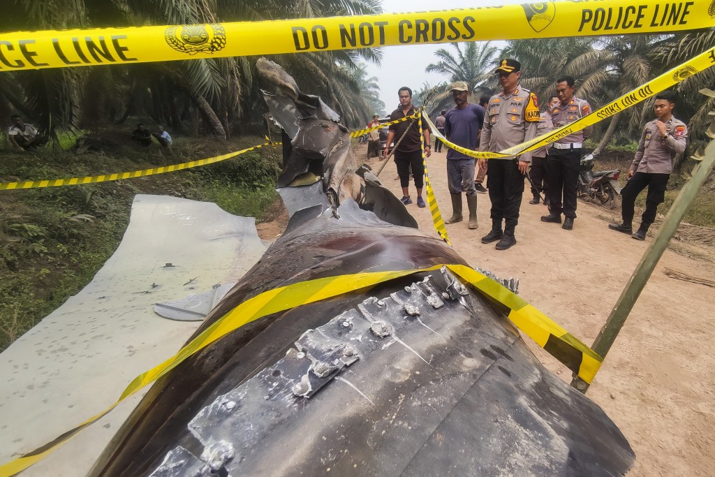 Photo by AHMAD SYIHAB / AFP  This picture taken on October 19, 2026 shows Indonesian police officers inspecting a large charred metallic fragment, suspected to be rocket debris, at an oil palm plantation in East Kotawaringin Regency, in Indonesia's Central Kalimantan province.