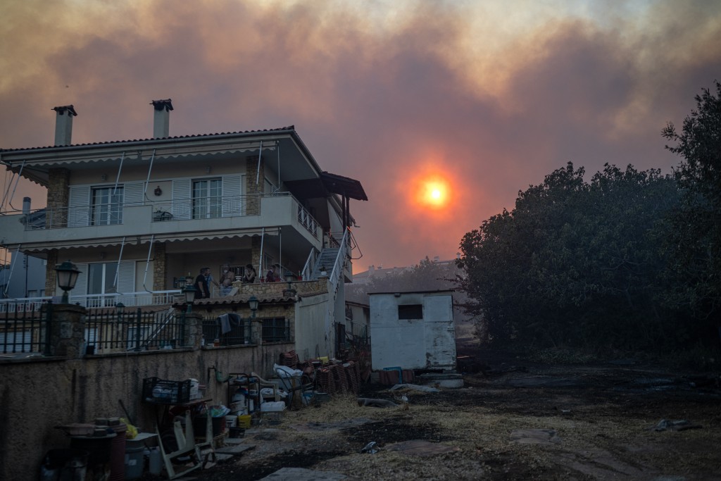Local residents cover their faces on the terrasse of a house during a wildfire in Kryoneri, near Athens on July 26, 2025. (AFP)