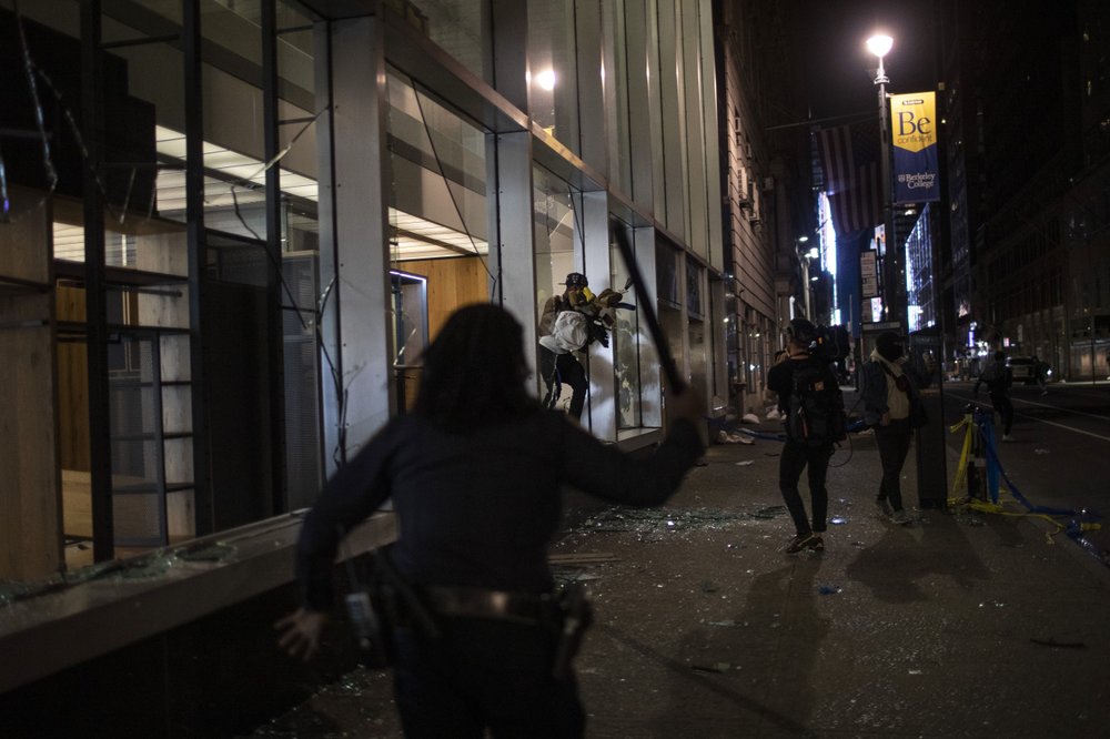 Police run towards people as they jump out of a store with items they took hours after a solidarity rally calling for justice over the death of George Floyd Monday, June 1, in New York. 